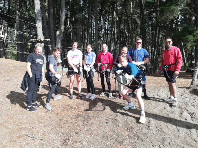 Seven students and two teachers in group photo with obstacle course safety gear on