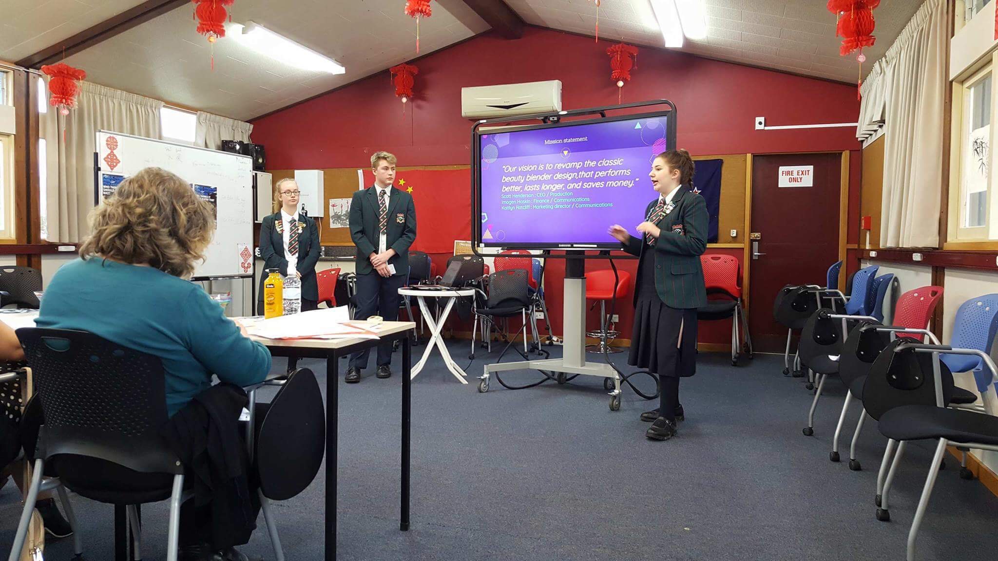 Three students presenting to teachers with a digital slideshow.