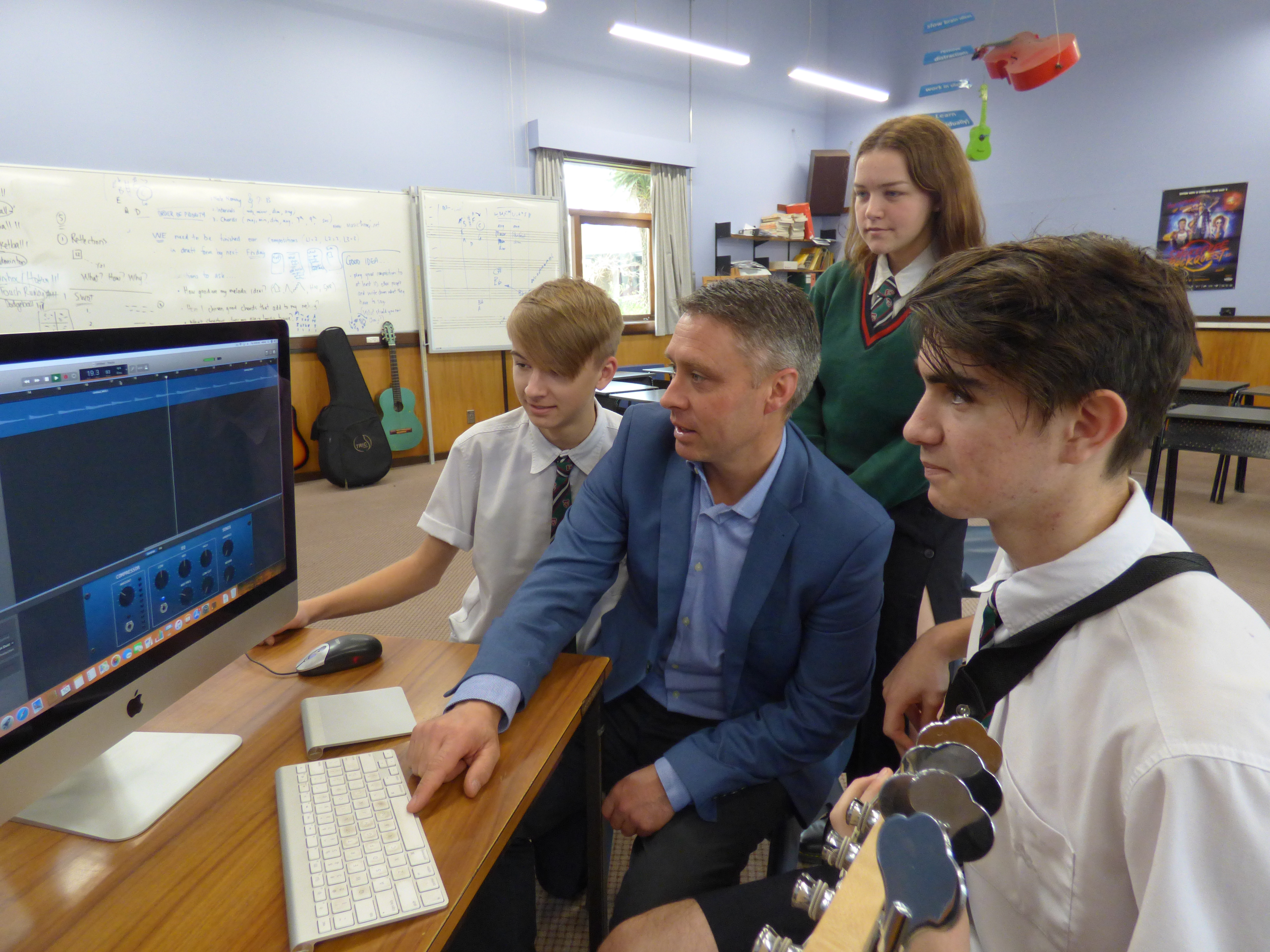 Teacher showing three students looking at a computer.